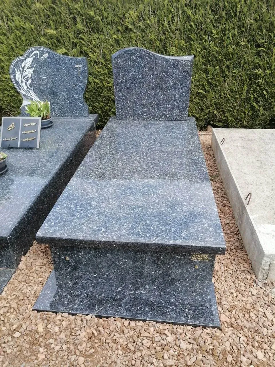 Tombe en granit bleu moucheté avec stèle gravée exposée sur sol gravillonné