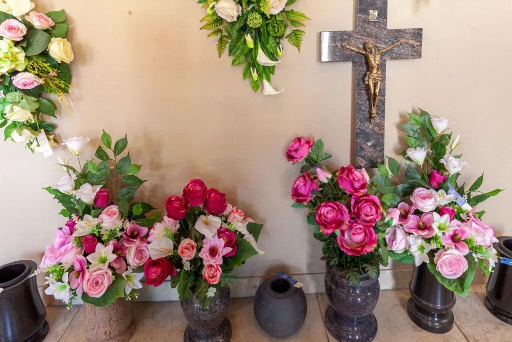 Compositions de fleurs artificielles et pots de fleurs de deuil posés au sol avec crucifix