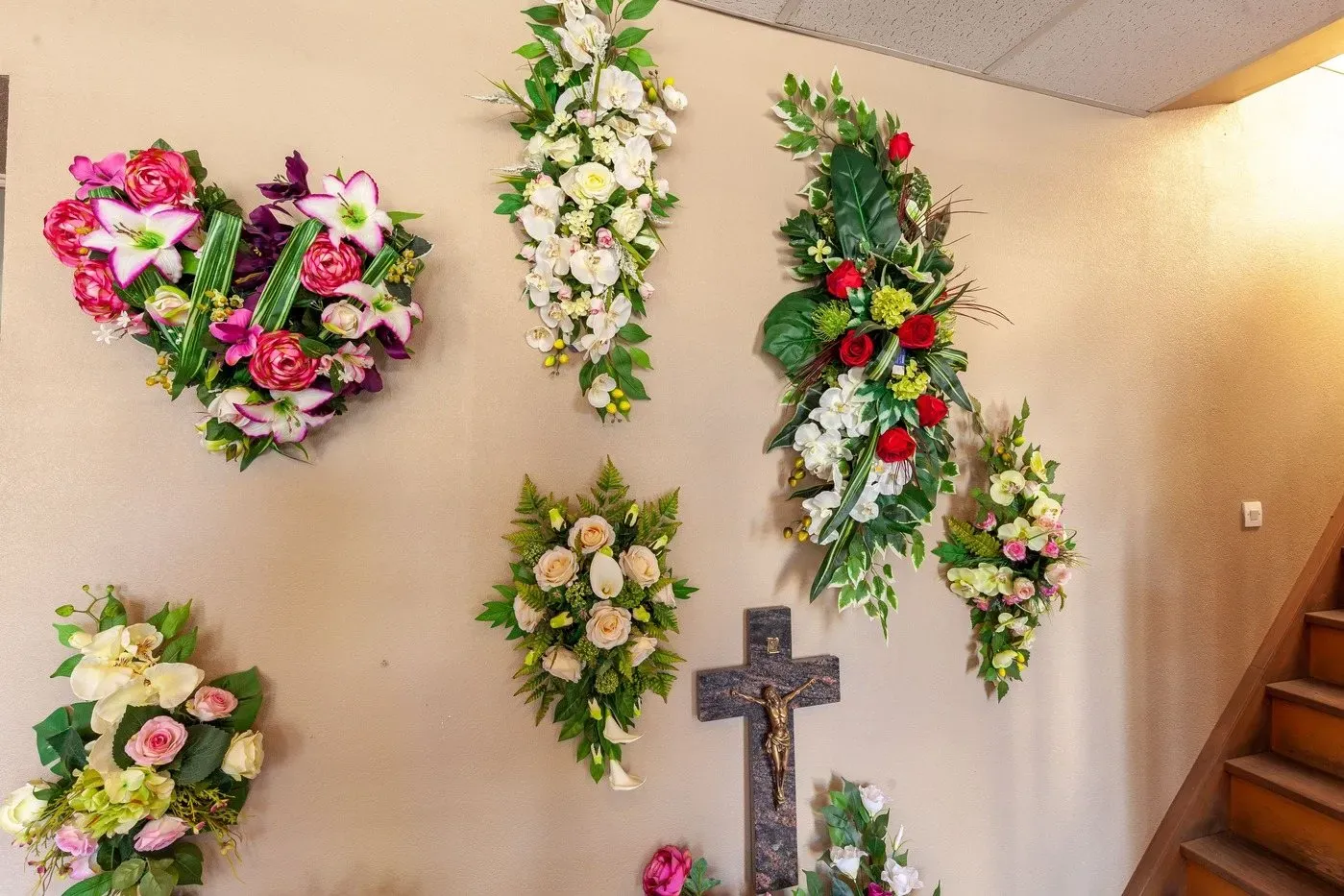 Exposition murale de compositions florales de deuil aux formes variées entourant un crucifix