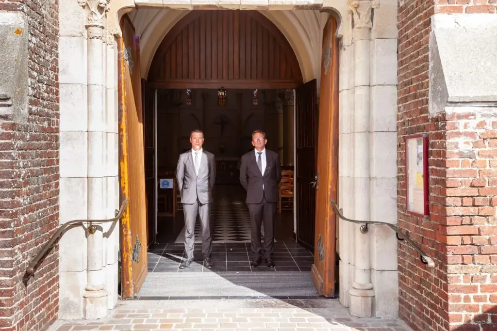 Deux porteurs funéraires en costume debout à l'entrée d'une église en briques